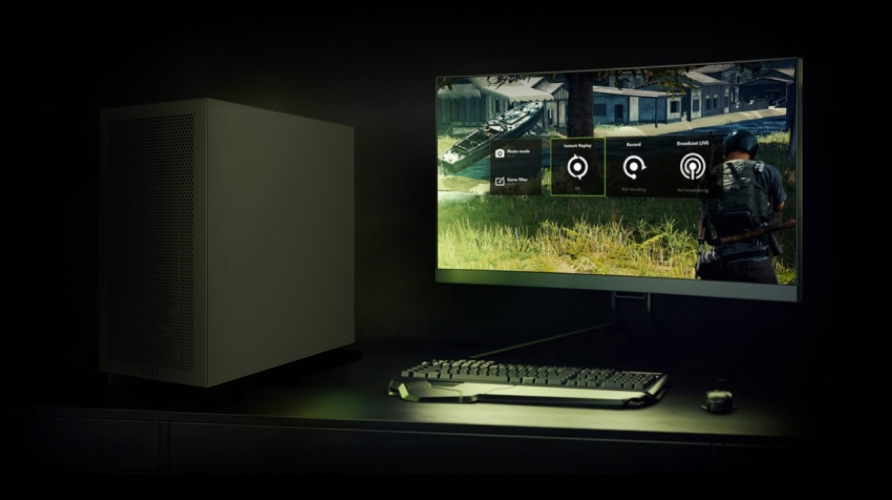 A desktop computer setup with a monitor displaying a video game, keyboard, mouse, and a PC tower on a dark desk in a dimly lit room.