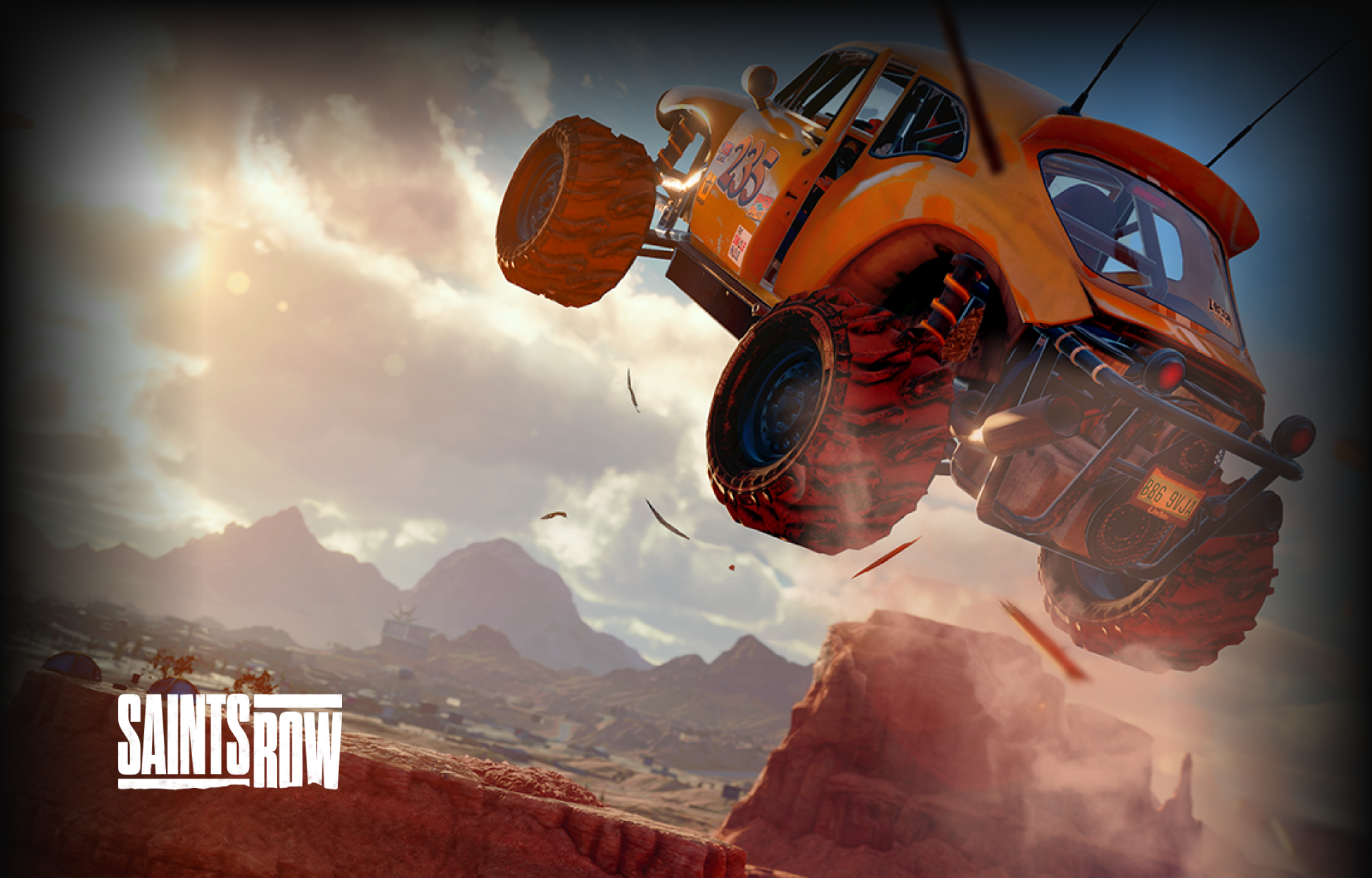 An off-road vehicle jumps over a desert canyon with dust flying, under a dramatic sky. The Saints Row logo appears in the lower left corner.