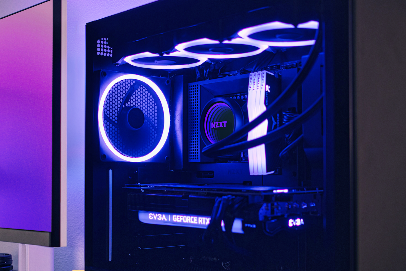 Sideshot of an NZXT case that looks through the clear, glass sidepanel. The shot is dimly lit, showcasing krakens with RGB and other RGB elements that light up the PC components and cables in the case.