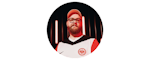 A bearded man wearing glasses, a red cap, and a white and red sports jersey with a circular logo stands in front of a background with vertical light bars.